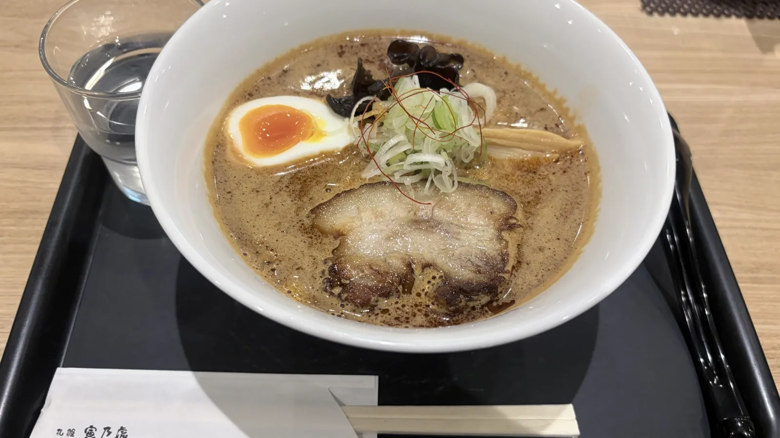 黒いトレーに乗った寅乃虎のスパイスらーめんと水のグラス。箸袋には札幌寅乃虎の文字