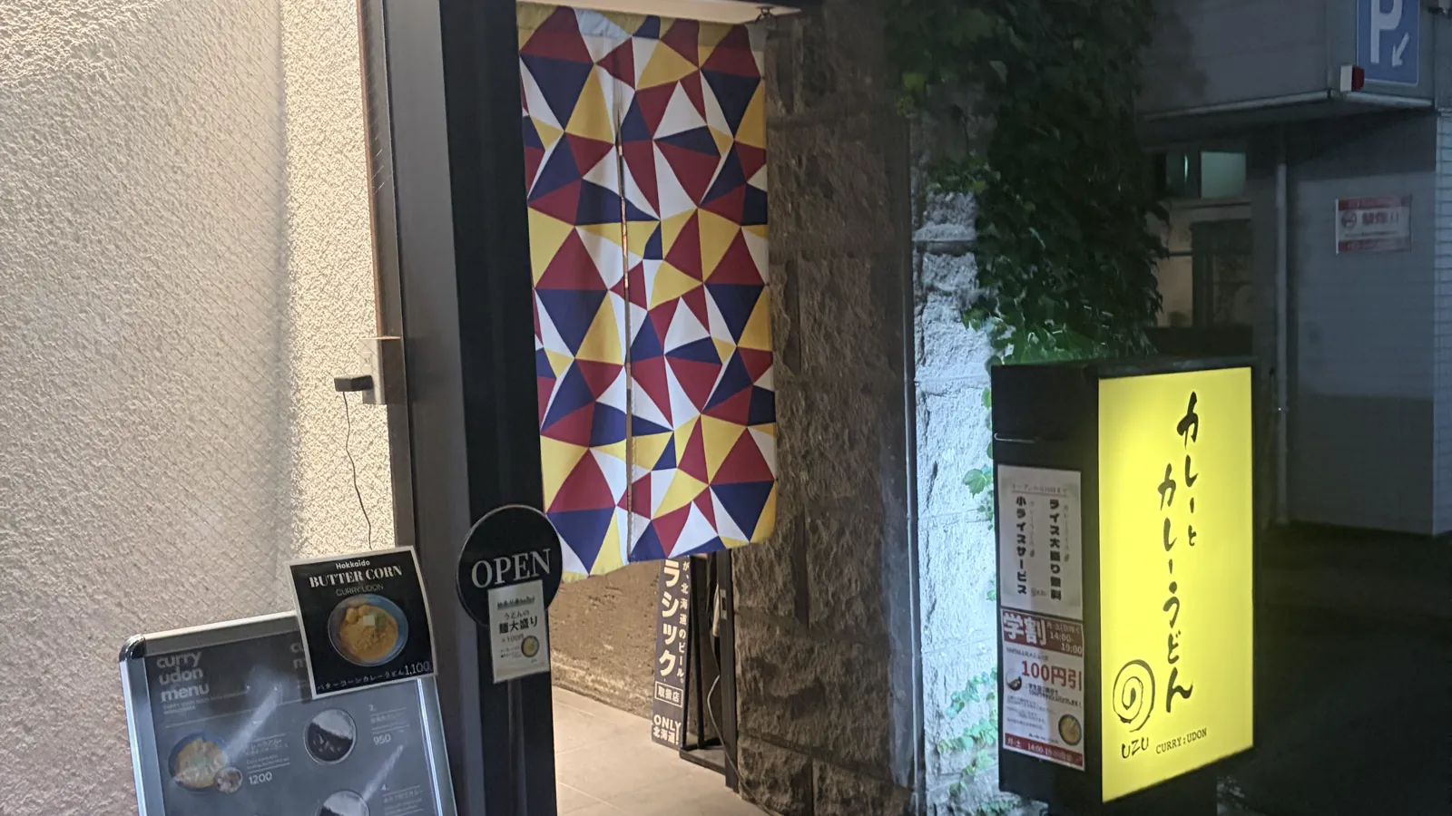 うずの入口。三角模様の暖簾とOPEN看板、黄色い電飾看板が並ぶ夜の外観