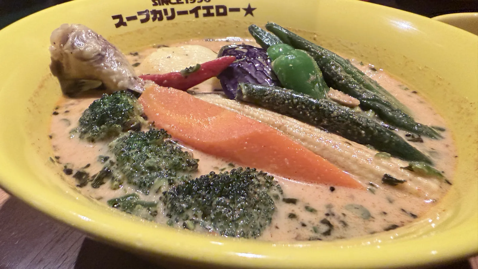 黄色い器に入ったチキン野菜カリーの寄り。クリーミーなスープにオクラやにんじん、ブロッコリーが浮かぶ