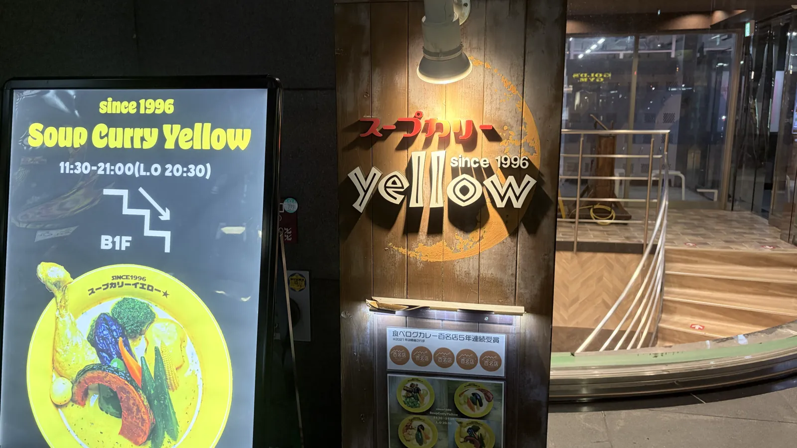 スープカリーイエローの入口。電飾看板と木の看板の横に地下1階へ下りる階段がある